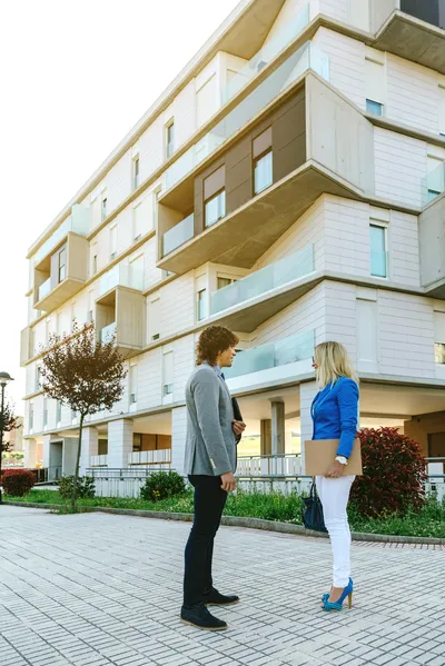 Fuera de unos condominios, hay dos personas que se encargan de la administración de condominios Dos personas fuera de unos condominios, hacen la administración de condominios